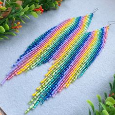 multicolored seed beaded earrings laying on top of a table next to plants