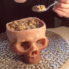 a woman eating cereal with a skull shaped bowl in front of her on a table