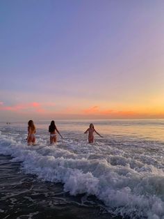 three girls are wading in the ocean at sunset