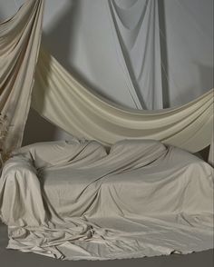 an unmade bed with white sheets and drapes on the wall behind it is shown