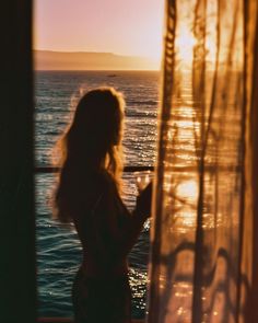 a woman standing in front of a window looking out at the ocean