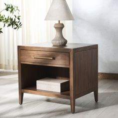 a nightstand with a lamp on top of it next to a plant in a room