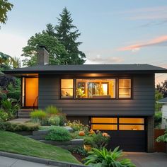 a modern house with lots of windows and plants in the front yard at night time