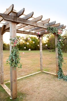 a wooden structure with flowers and greenery hanging from it's sides in the middle of an open field