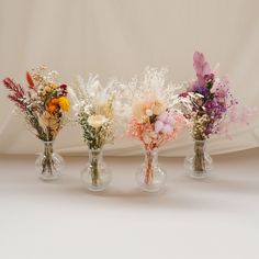 three vases filled with different types of flowers on a white tableclothed surface