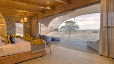 a bedroom with a large bed and wooden floors in front of an open window that looks out onto the plains