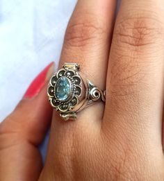 a woman's hand holding a ring with a blue stone in the center and filigrees on it