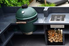 an outdoor grill with firewood in it and a large green egg sitting on top