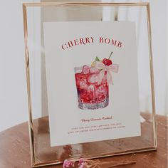 a cherry bomb cocktail in a glass with ice and cherries on the rim next to a sign