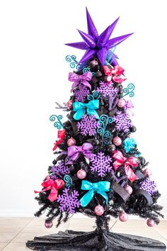 a decorated christmas tree with purple, blue and pink bows on it's top