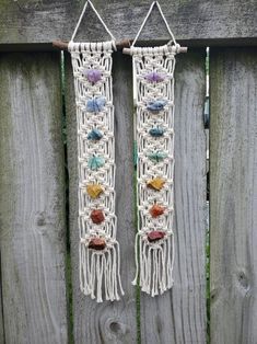 two macrame wall hangings with beads and stones in them on a wooden fence