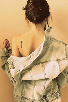 a woman with a cross tattoo on her upper back shoulder and arm, holding onto a jean jacket