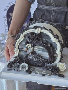 a woman is holding a cake decorated with an image of a dragon and roses on it