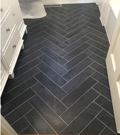 an image of a bathroom with black tile on the floor and white cabinets in the background