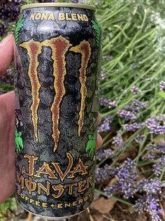 a person holding up a can of monster energy drink in front of some lavender flowers