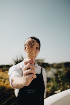 a man holding an ice cream cone in front of his face with the sky behind him