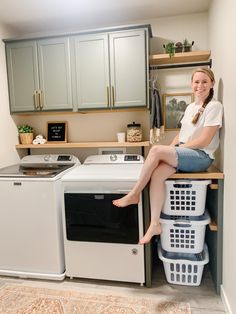 a woman sitting on top of a washer and dryer in a laundry room