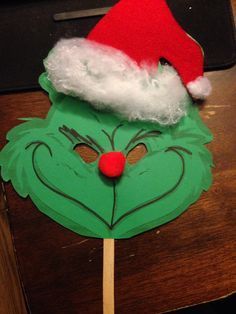 the grin face is made out of green paper and has a red santa hat on it