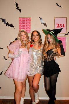 three girls dressed up in costumes posing for the camera with bats on the wall behind them