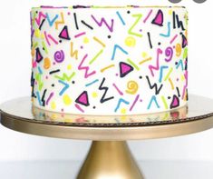 a white cake with multicolored sprinkles is on a gold plate