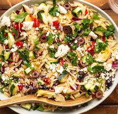 a bowl filled with pasta and vegetables on top of a wooden table