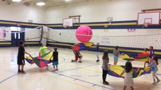 a group of people holding kites in a gym with balls on the floor and net