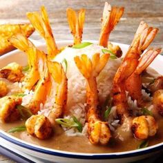 a white bowl filled with rice and shrimp on top of a wooden table next to fries