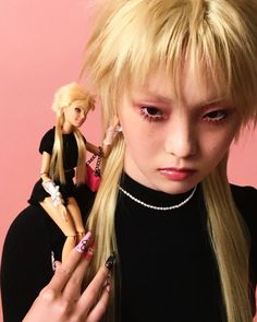 a woman with blonde hair and pink eyes holding a doll