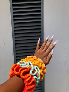 a woman's hand with multicolored manicures holding onto a colorful crocheted bracelet