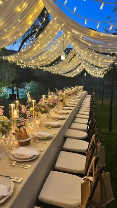 a long table is set with white linens and place settings for an outdoor dinner