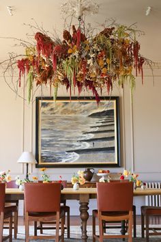 a dining room table with chairs and a painting hanging over it's head above the table