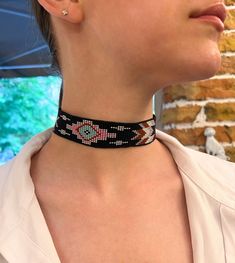 A black beaded choker with a geometric pattern, featuring vibrant elements in turquoise, pink, white, and brown tones. The piece is adorned with silver-colored metal elements and an adjustable chain, allowing you to customize the size to your preference. An excellent choice for creating a stylish and original look. Made of Czech beads. Hypoallergenic clasp. Length 12.8 inches (32.7 cm)+Chain extension 2 inches (5cm). Taking the clasp into account. Width 1.1 inches (2.9 cm). If you want this chok Southwestern Black Beaded Necklaces For Festivals, Southwestern Black Beaded Necklace For Festivals, Black Southwestern Necklaces For Festivals, Black Southwestern Necklace For Festival, Pink Bohemian Choker For Festivals, Southwestern Style Black Necklace For Festival, Southwestern Style Black Necklace For Festivals, Handmade Southwestern Style Choker, Black Bohemian Choker