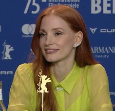 a woman with long red hair sitting at a table in front of a microphone and bottle of wine