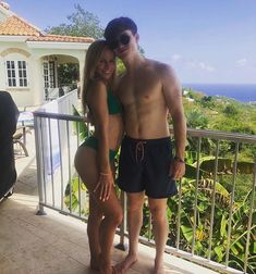 a man and woman posing for a photo on a balcony overlooking the ocean in front of a house