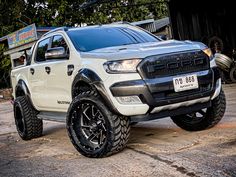 a white pickup truck parked in front of a building with large tires on it's rims