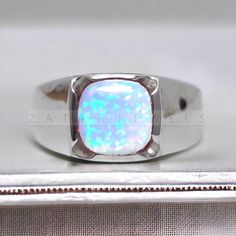 an opalite ring sits on top of a silver box with a white background