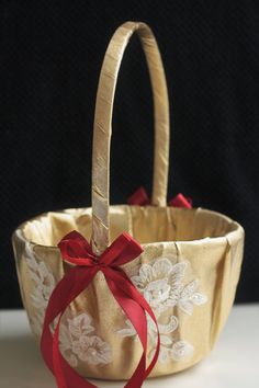 a gold basket with red ribbon tied around the handle and flowers on it, sitting on a white surface