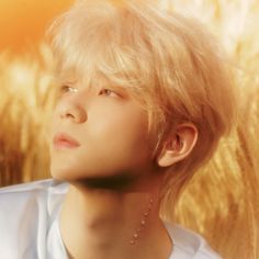 a young man with blonde hair wearing a white shirt and silver necklace looking to the side