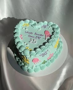 a heart shaped birthday cake on a white plate with silver cloth in the back ground