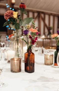 the table is set with candles and vases filled with colorful flowers in glass bottles