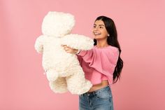 a woman holding a white teddy bear in her hands and smiling at the camera on a pink background