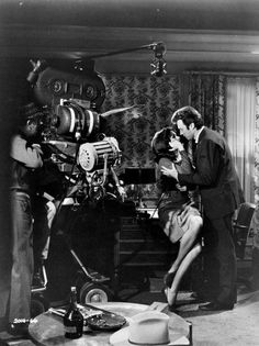 black and white photograph of two people in front of a movie camera, one holding a woman's head