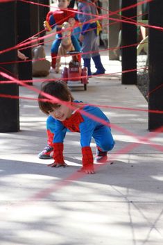 a little boy dressed as spider man playing with some kind of rope on the sidewalk