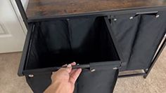 a person is holding the bottom section of a black storage cabinet with two doors open