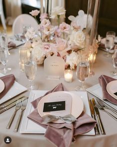 the table is set with white and pink flowers, silverware, and napkins