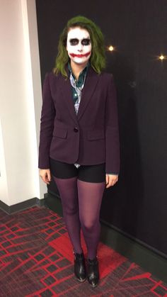 a woman dressed up as the joker in a suit and tie, standing next to a wall