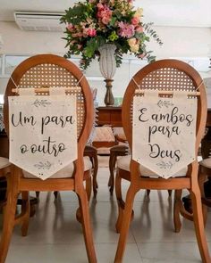 two wooden chairs sitting next to each other in front of a vase with flowers on it