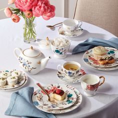 a white table topped with plates and cups filled with desserts next to pink flowers