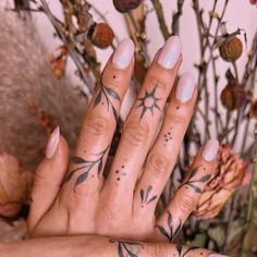 a woman's hand with tattoos on it and flowers in the background, holding up her fingers