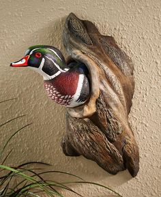 a wood duck head mounted on the side of a wall next to a potted plant